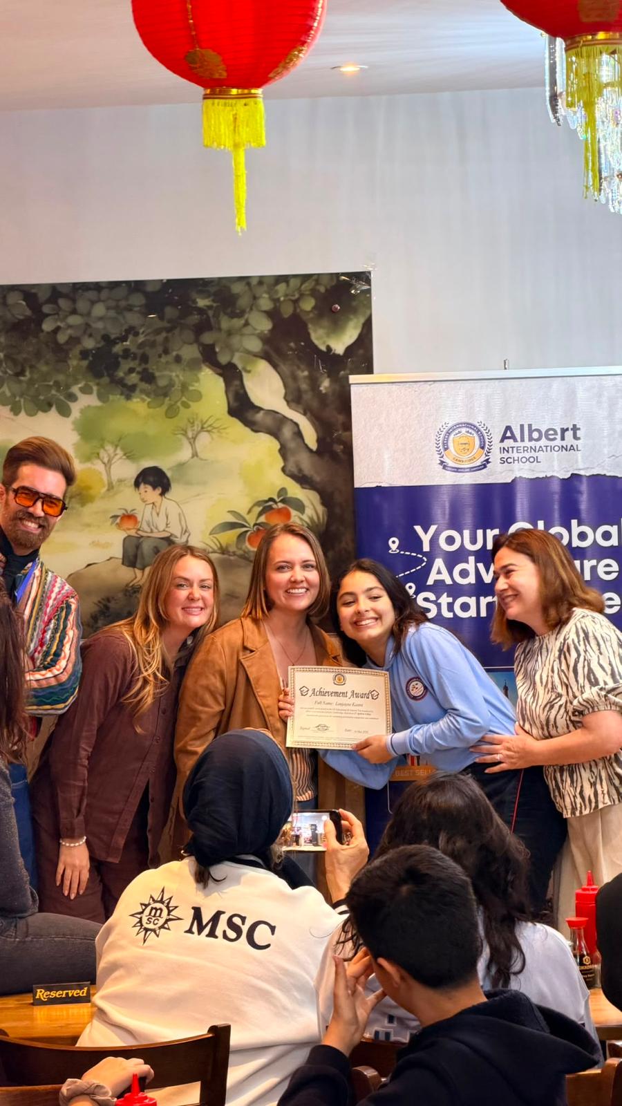 Student from Alexander Flemming receives English Program Certificate of Completion next to her teacher and Albert International School staff